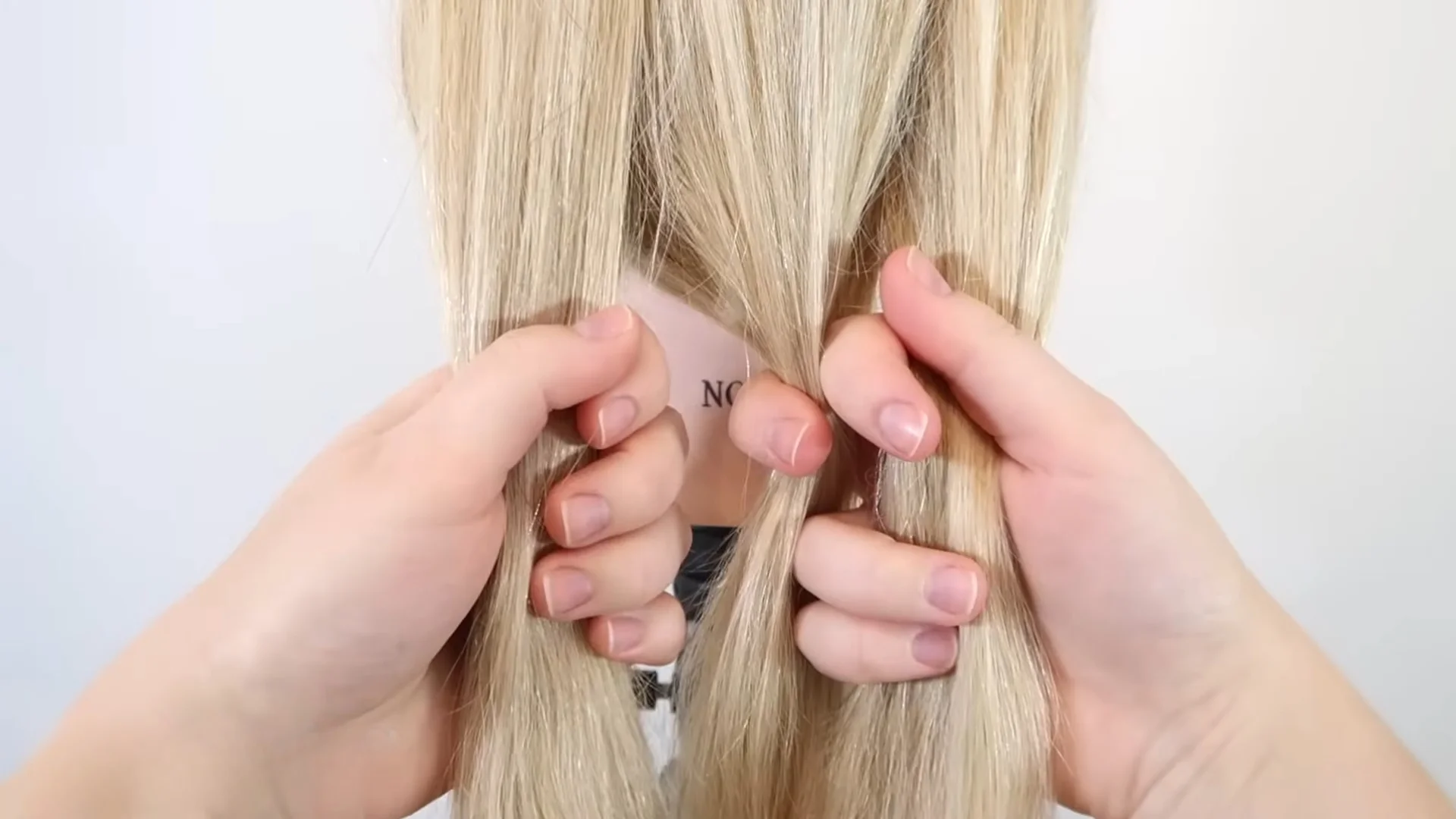 Three separate sections of blonde hair held in both hands, showing the correct starting grip before crossing strands into a basic braid.