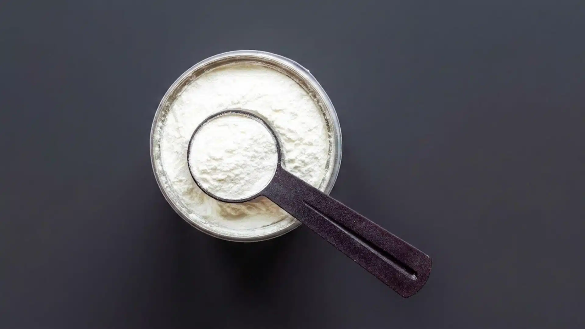 Top-down view of a creatine scoop in a tub, isolated on a dark gray background