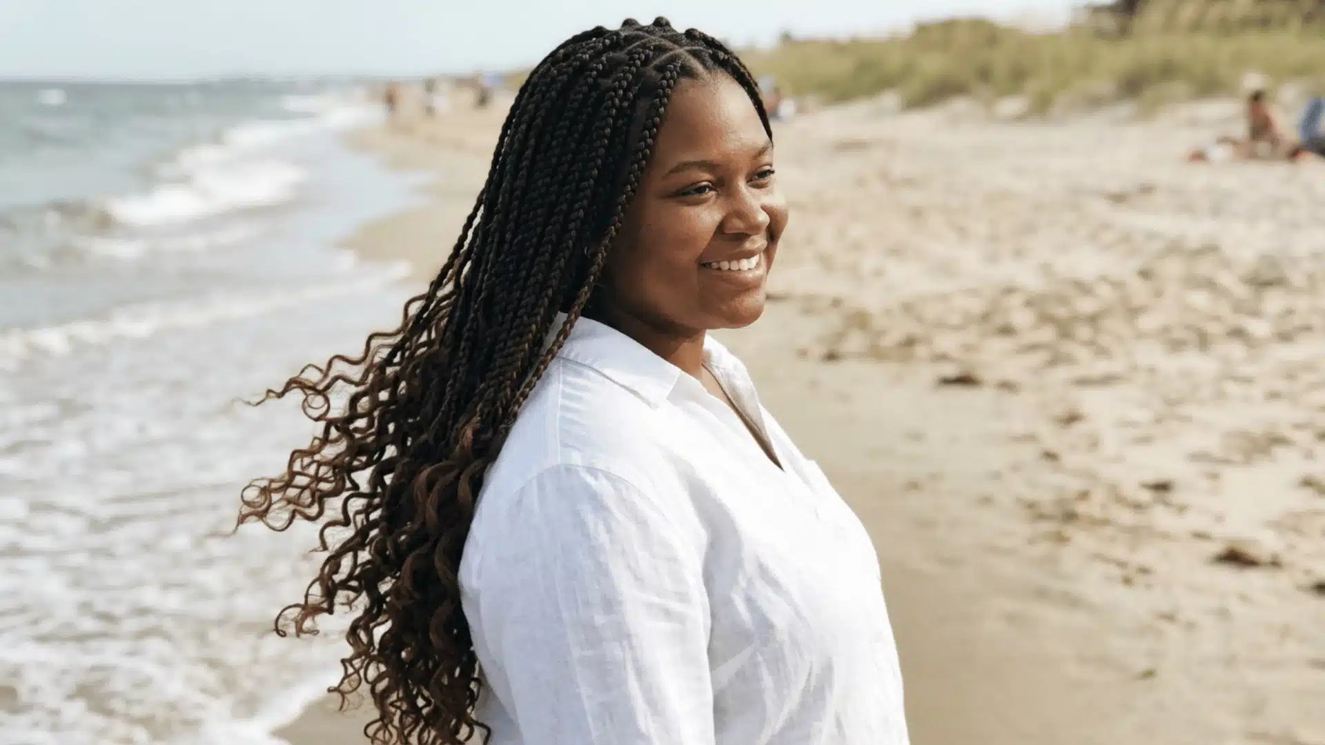 Waist-length boho braids with loose curly ends and natural dark brown color on a Black woman at the beach