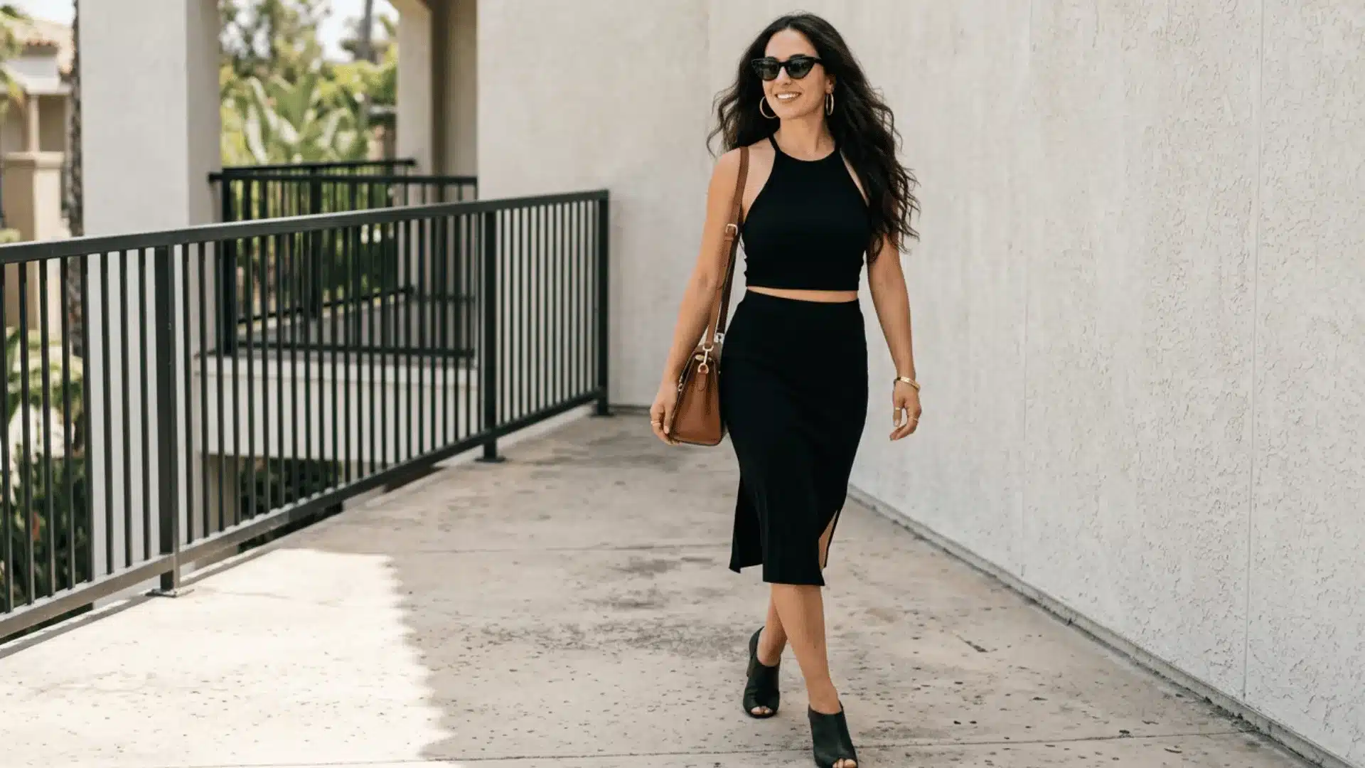 Woman in a black halter crop top and midi skirt walking outdoors in a chic summer date-night outfit