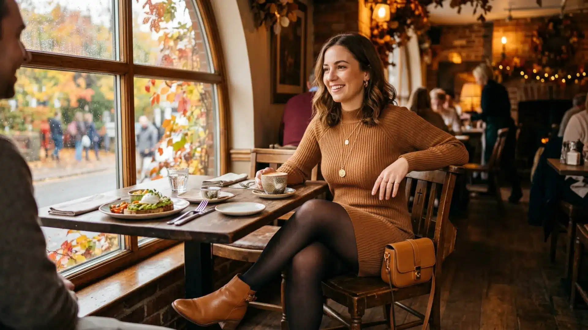 Woman in a ribbed caramel sweater dress and tan ankle boots seated at a window table for fall brunch