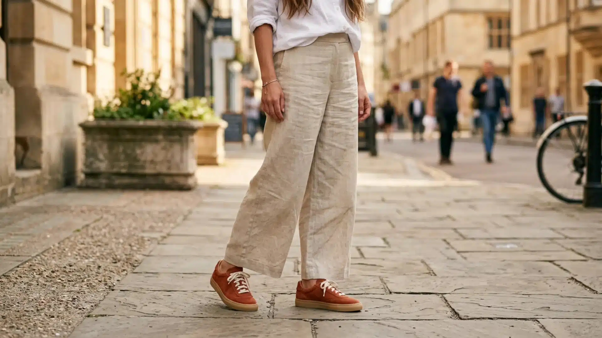 Woman in wide-leg linen trousers wearing suede Adidas Gazelle sneakers in terracotta on sidewalk