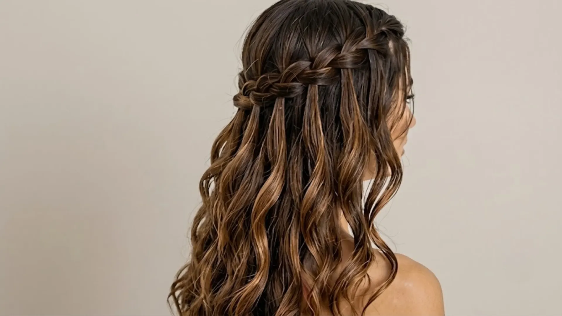 Woman with long wavy hair styled in a half-up waterfall braid from the side view