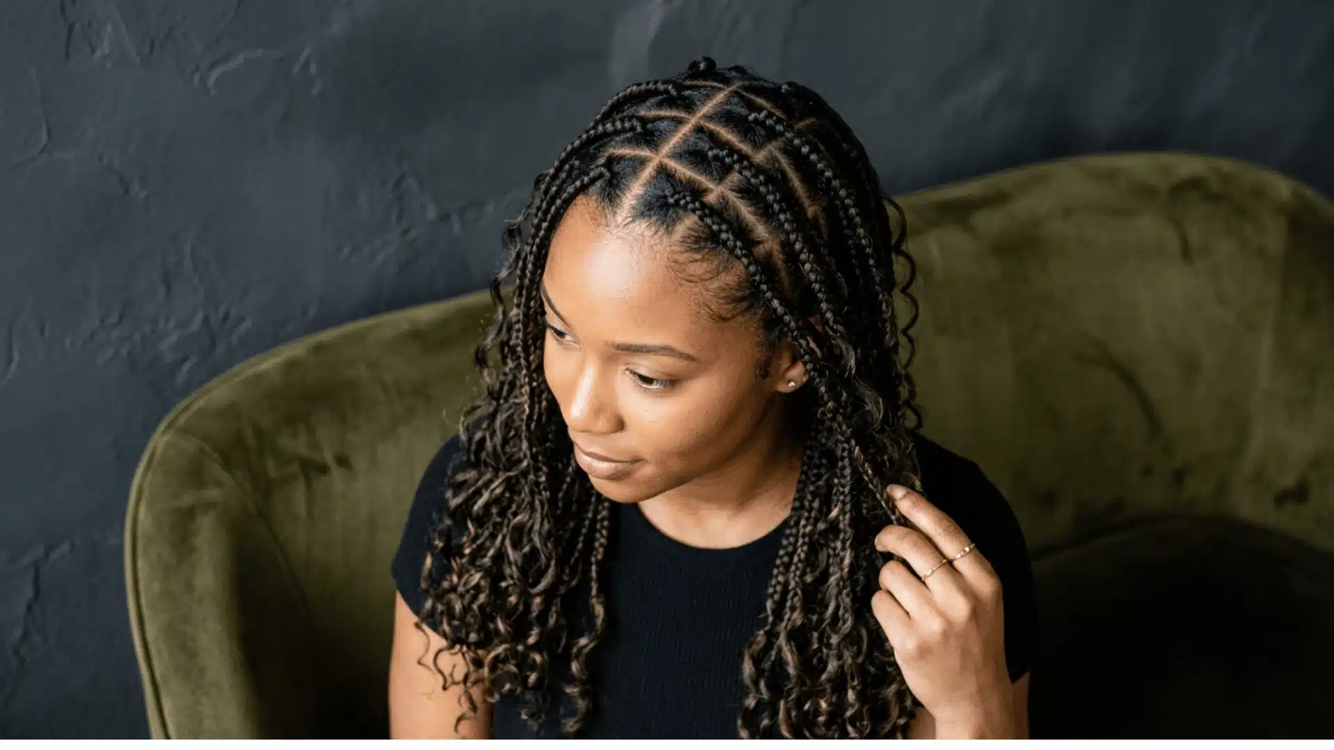 Woman with triangle-parted boho braids showing detailed root sections against a deep charcoal background