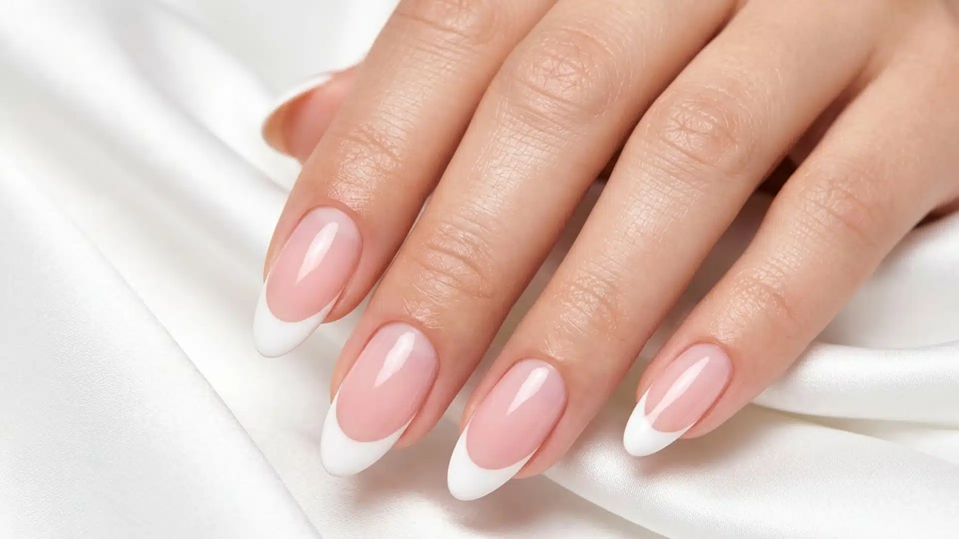 A classic French manicure on almond-shaped nails against white satin