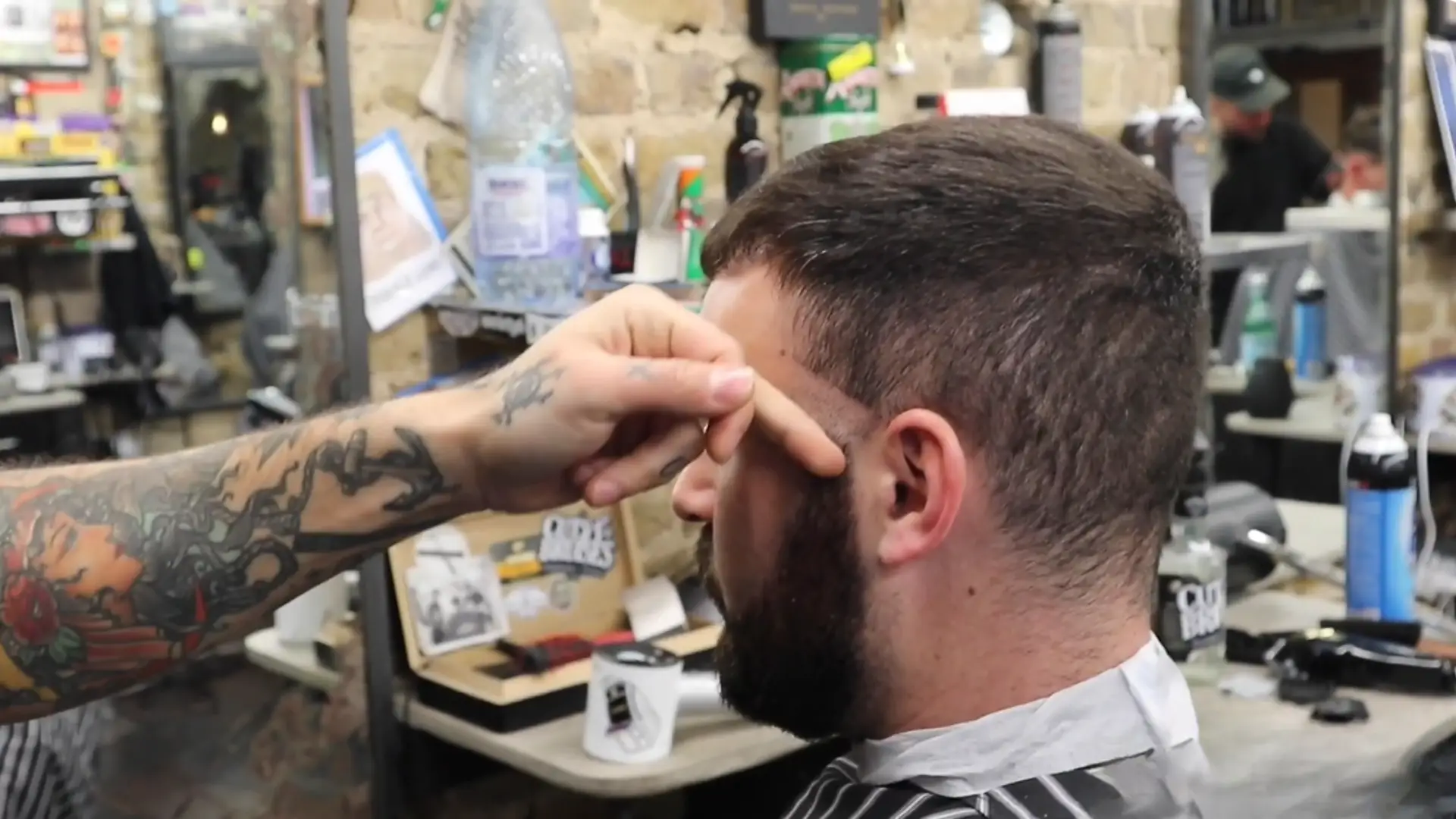 Barber shaping hairline with finger guide on client in barbershop, close up of fade haircut and beard