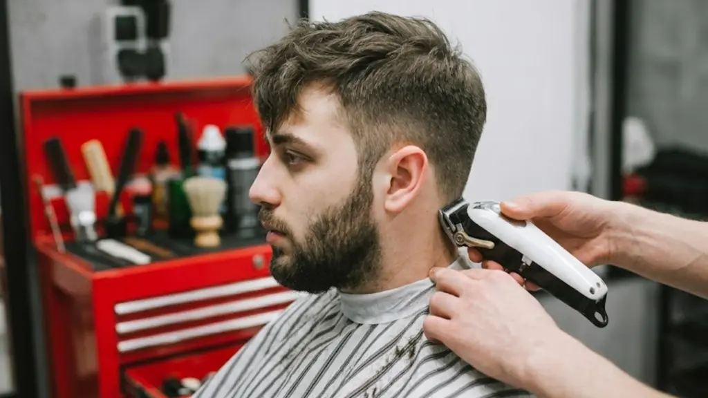 Barber trimming a man's low taper fade with clippers in a modern shop near grooming tools