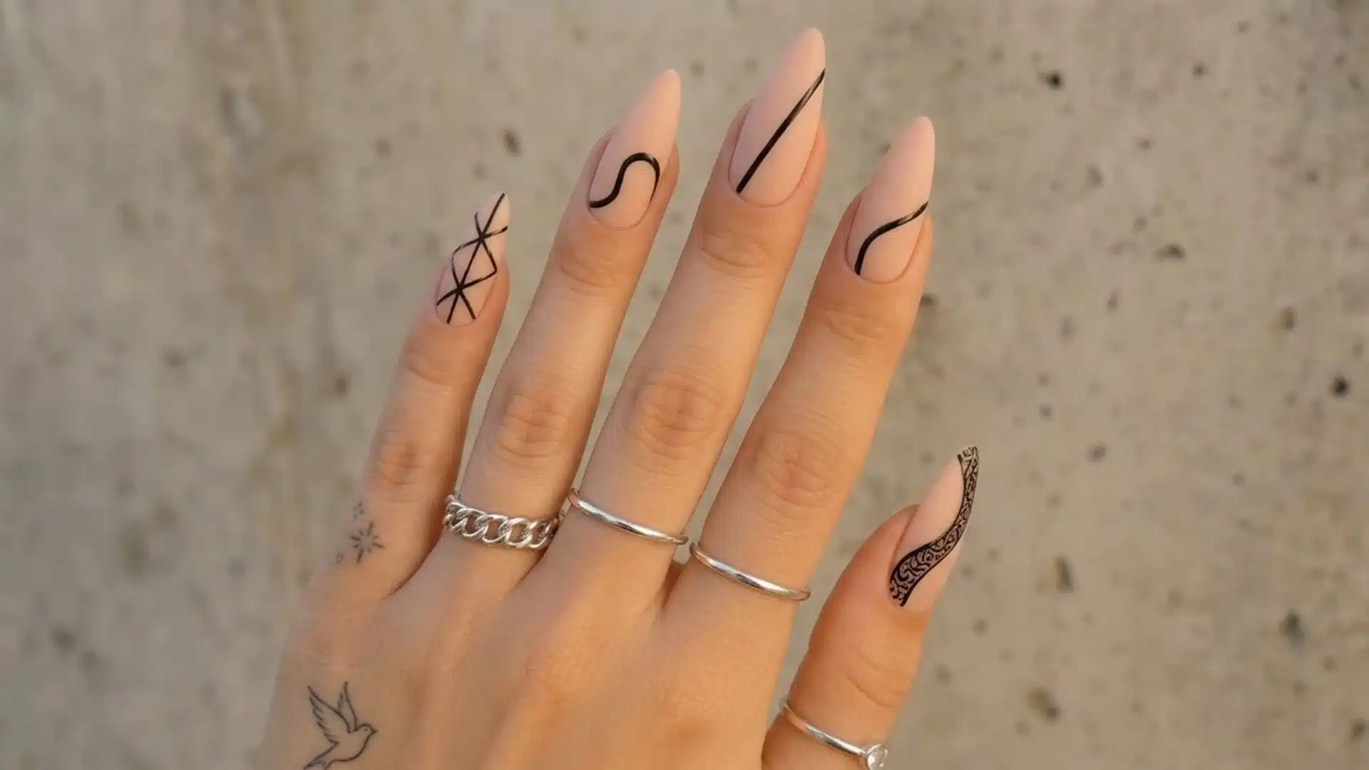 black and nude abstract almond nails with minimal line art design on hand against textured background