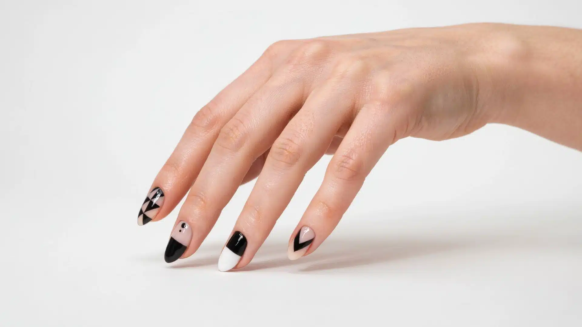 black and white geometric almond nails with nude accents on a natural hand against a white background