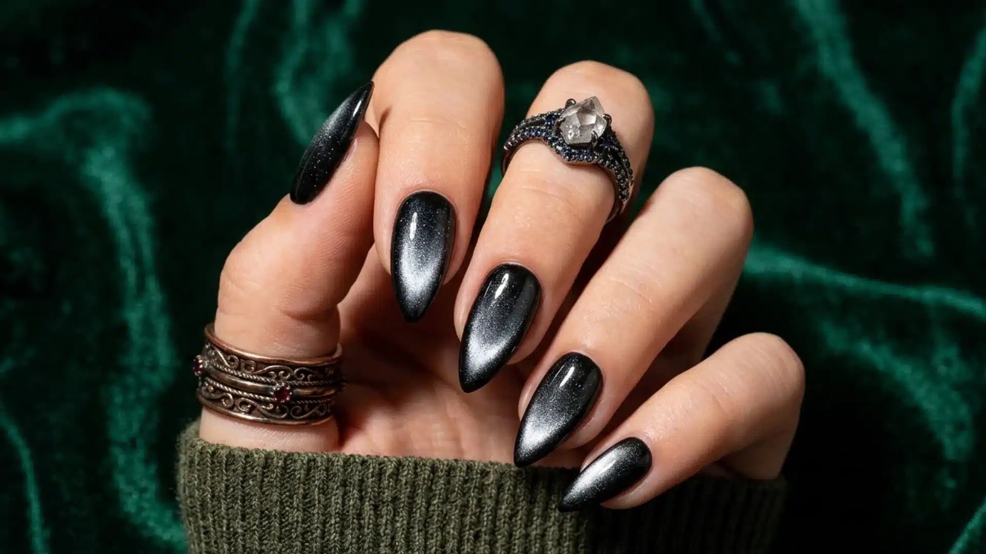 black cat eye almond nails with magnetic shimmer effect and glossy finish on hand against green background