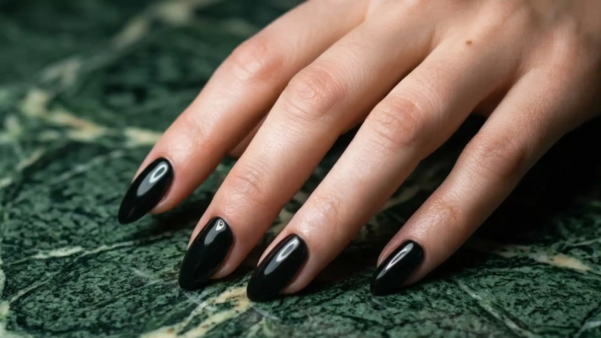 black chrome almond shaped nails with glossy finish on hand over textured marble surface