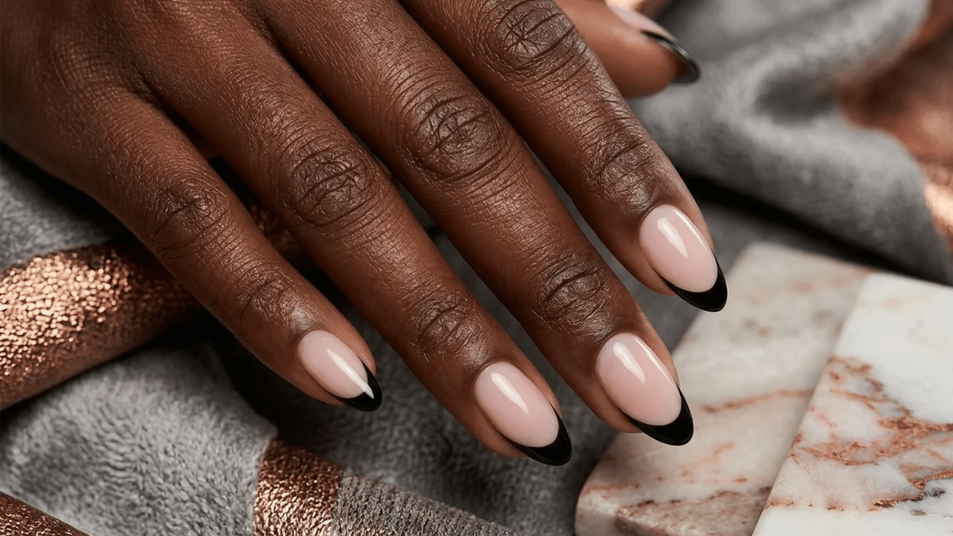 black french tip almond nails with nude base polish on dark skin hand over marble and fabric background