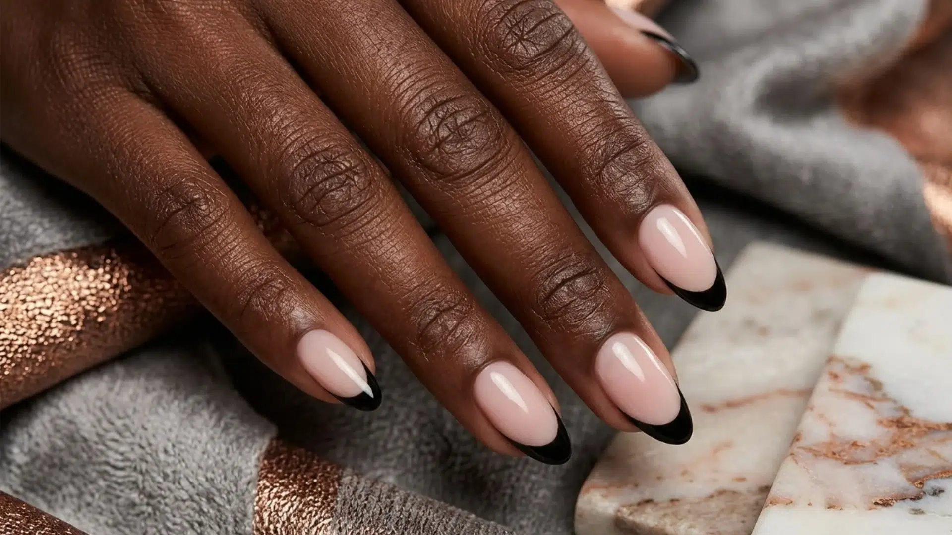 black french tip almond nails with nude base polish on dark skin hand over marble and fabric background