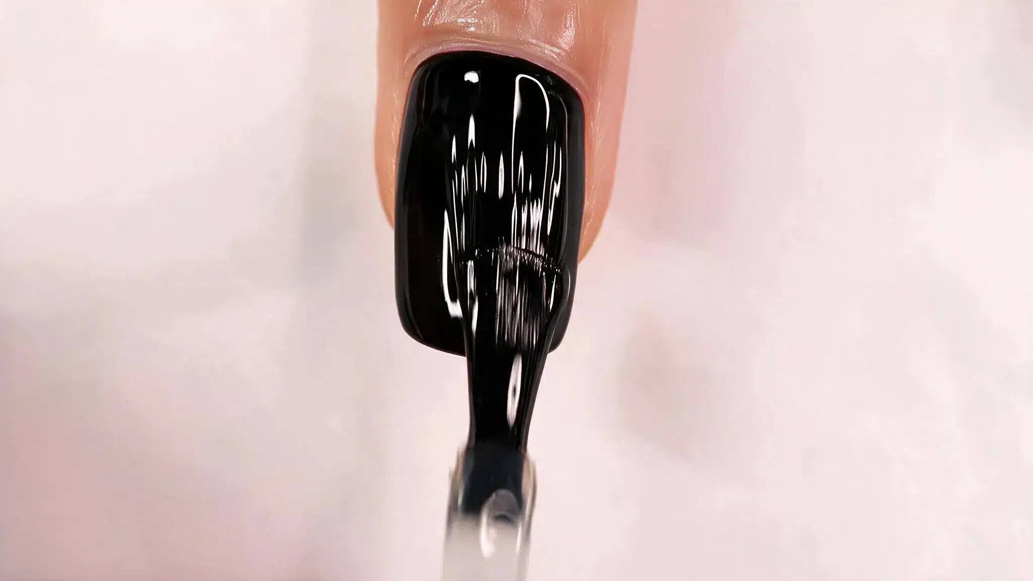 black nail polish application on fingernail with glossy finish and brush close up
