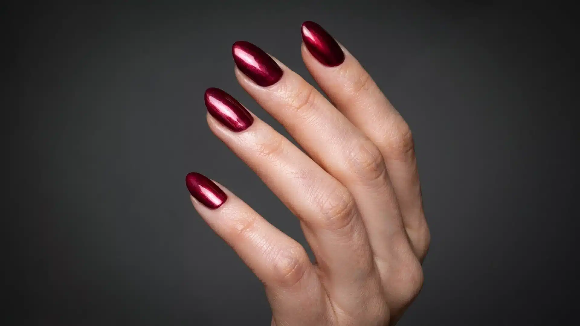 burgundy chrome almond nails with a glossy metallic finish on a natural hand against a dark background