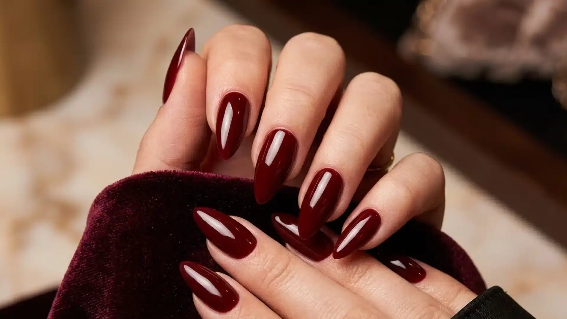 burgundy glossy almond shaped nails on hands with rich dark red polish and reflective finish