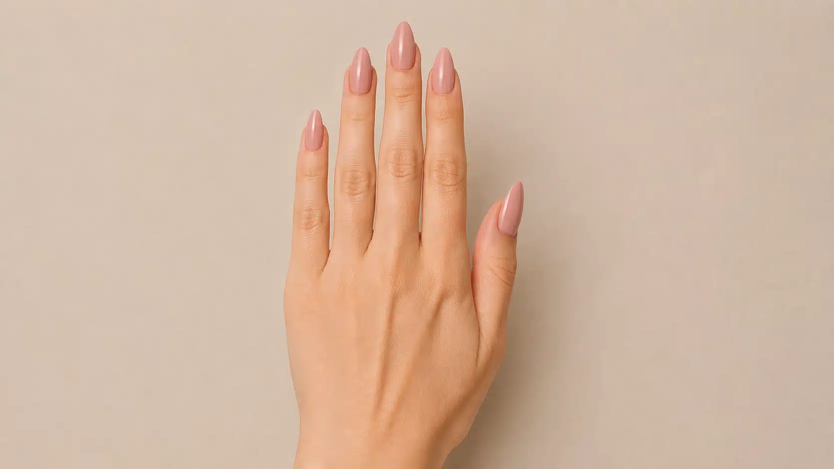 Close-up of a hand with glossy nude-pink almond-shaped nails featuring smooth curved edges and softly tapered rounded tips on a beige background