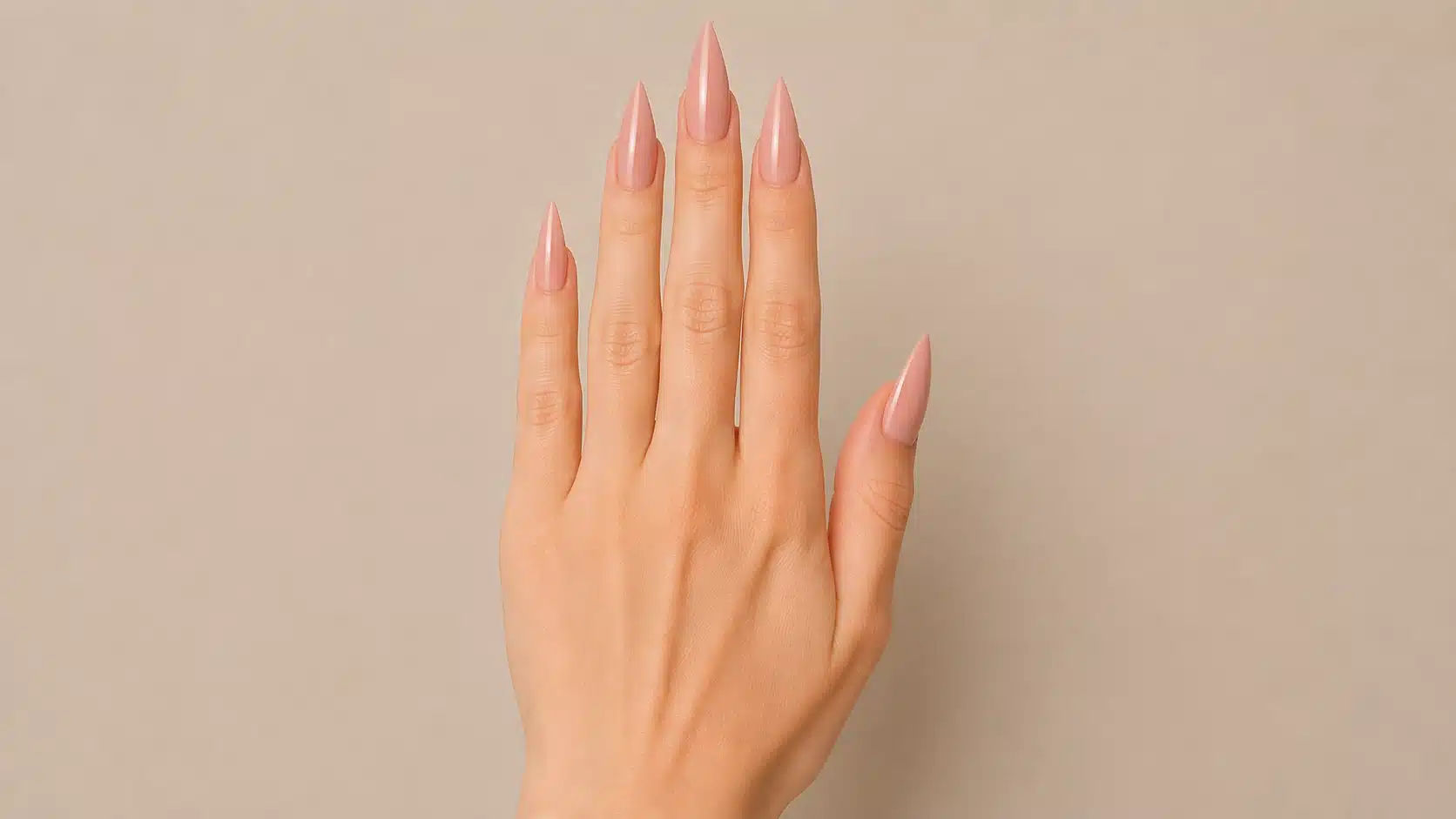 Close-up of a hand with glossy nude-pink stiletto nails featuring long, sharply tapered sides and pointed tips