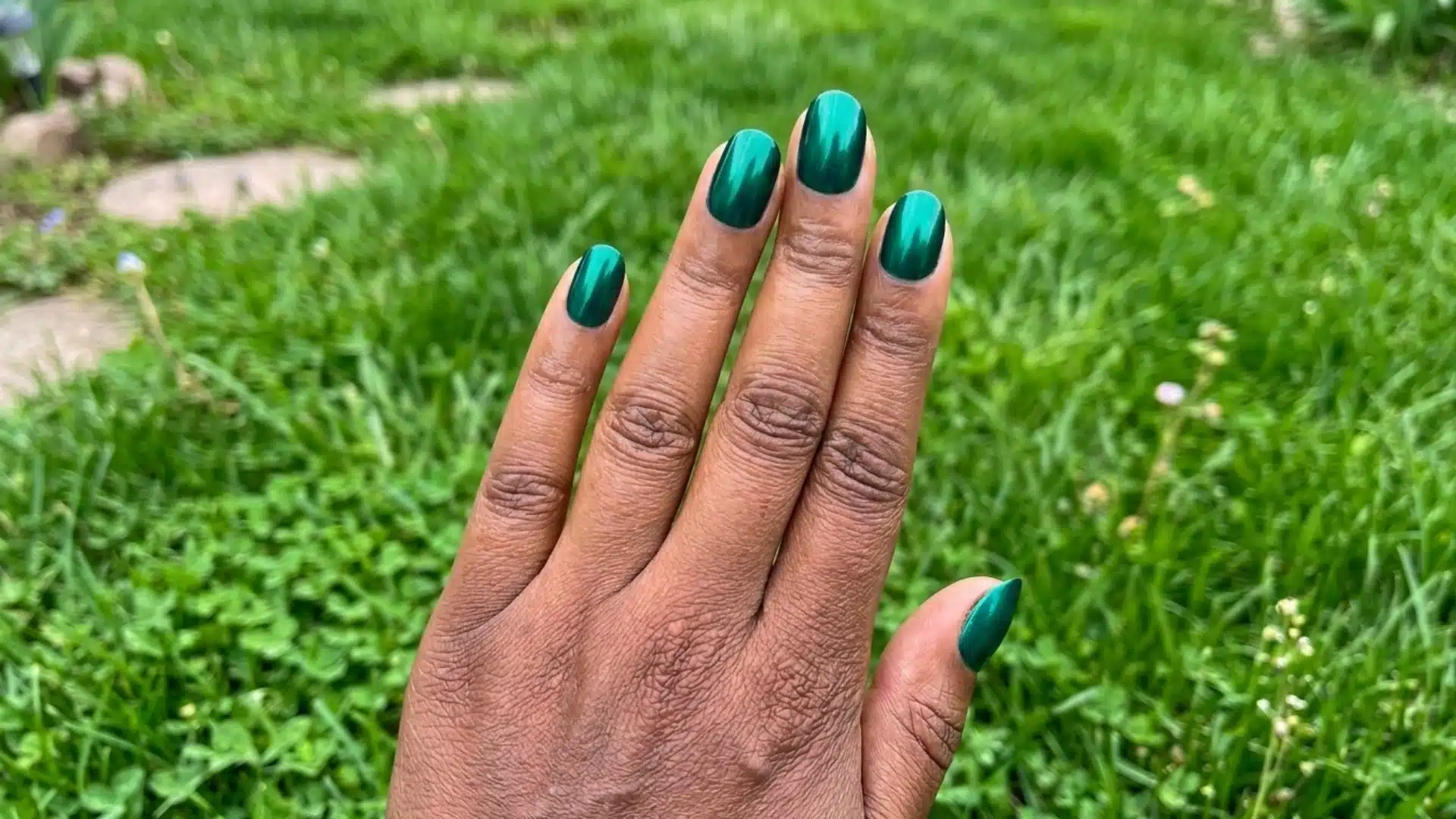 emerald green velvet almond nails with glossy finish on hand against blurred grassy outdoor background