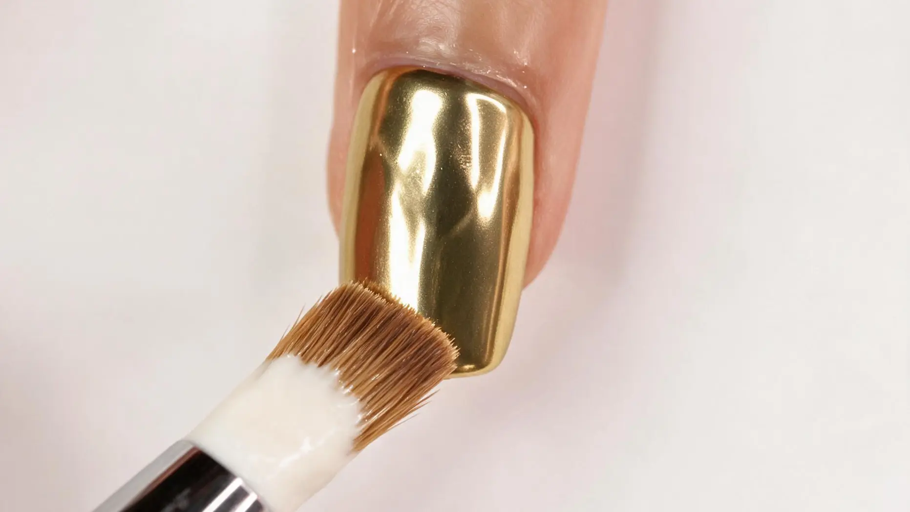 gold chrome nail being cleaned with a brush during manicure preparation close up