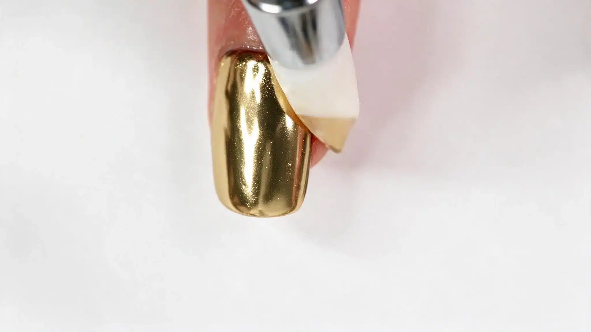 gold chrome nail polish application on fingernail with glossy metallic finish close up
