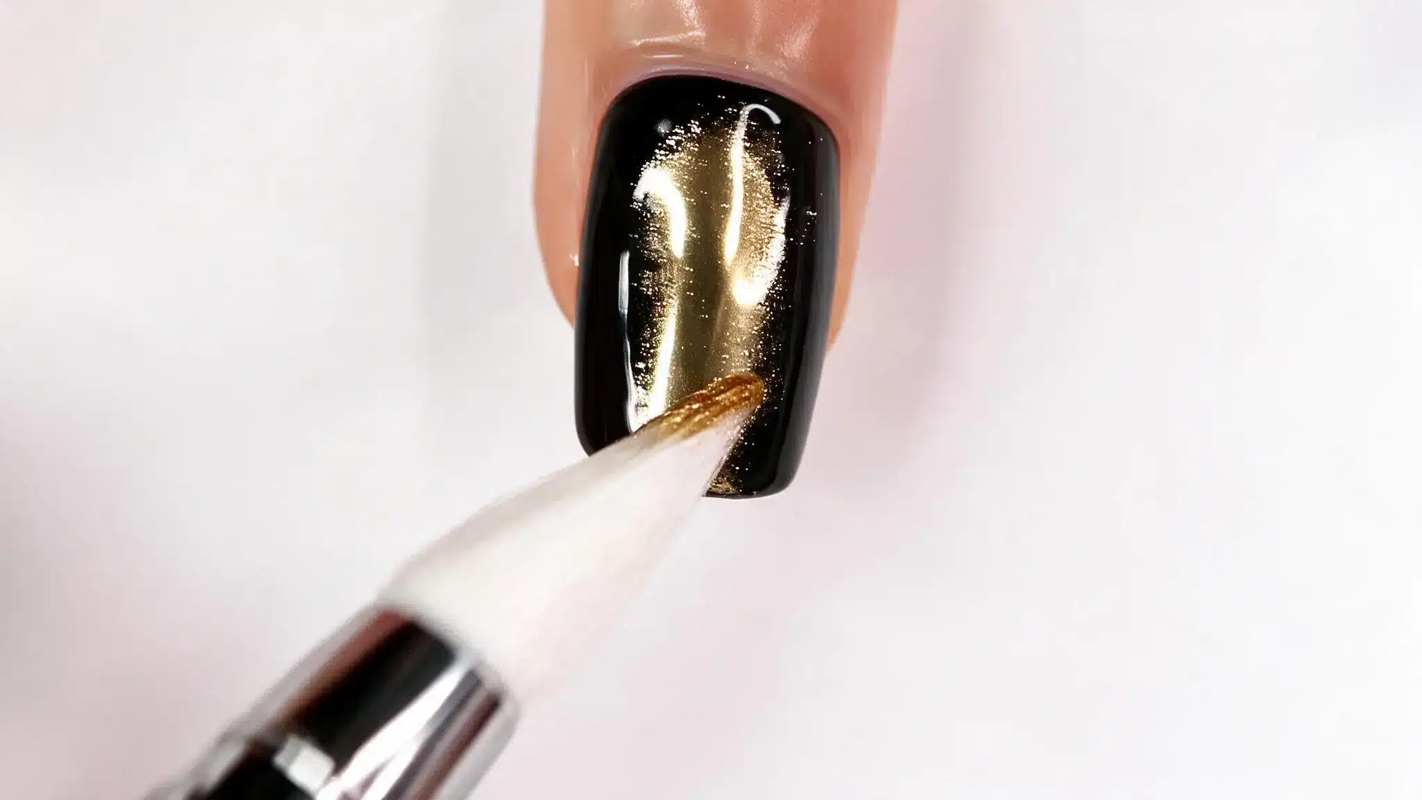 gold nail polish brush applying glitter design on glossy black fingernail close up