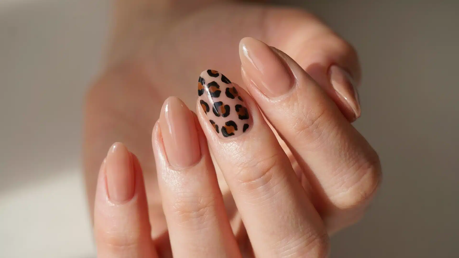 leopard print accent almond nails with glossy nude polish and black brown spots on a natural hand