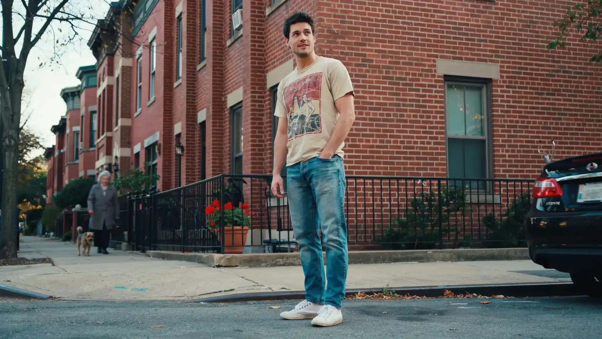 man wearing 80s graphic t shirt with faded jeans and white sneakers on city street