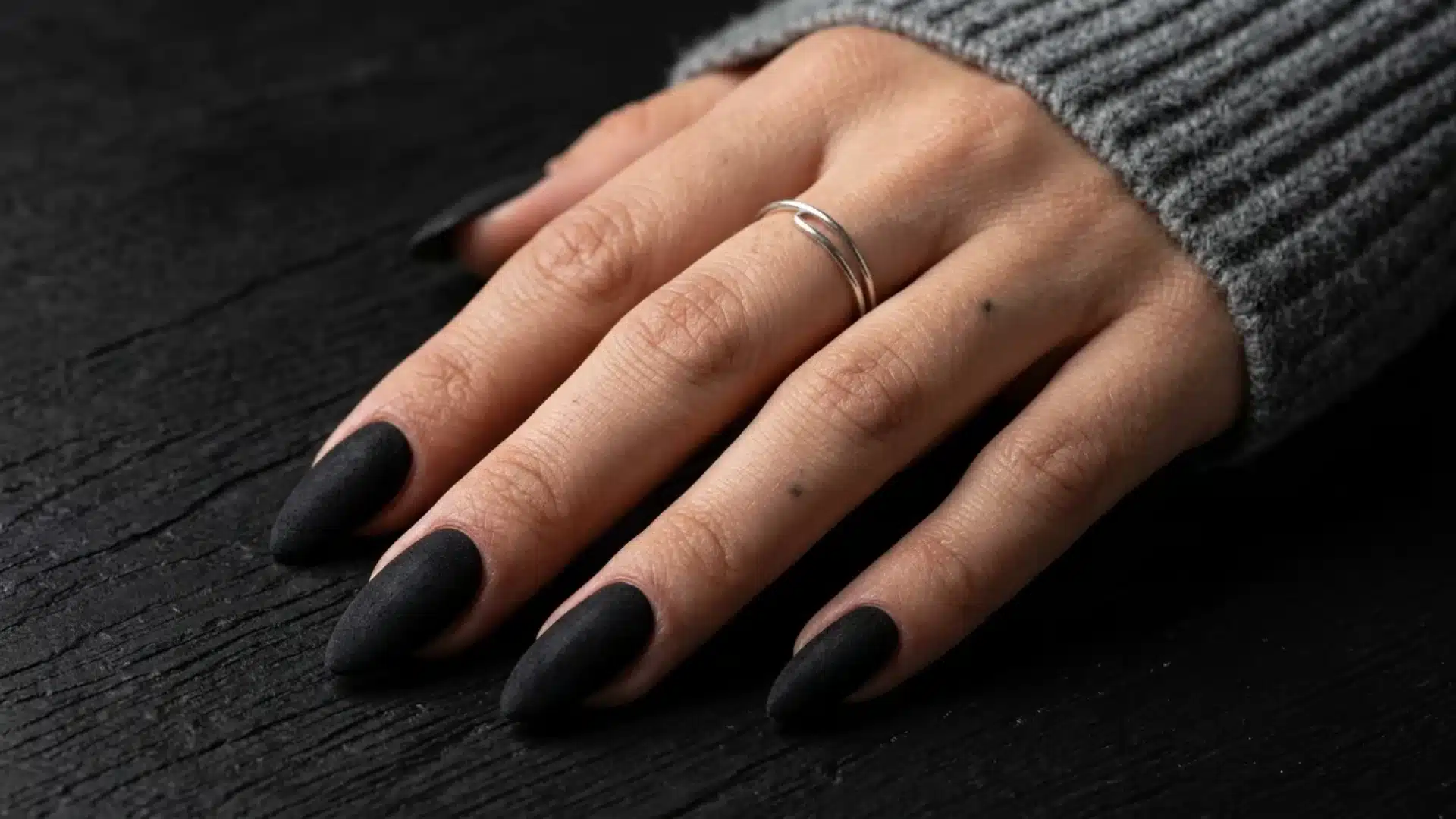 matte black almond shaped nails on hand with soft texture and dark background for a minimal nail design look