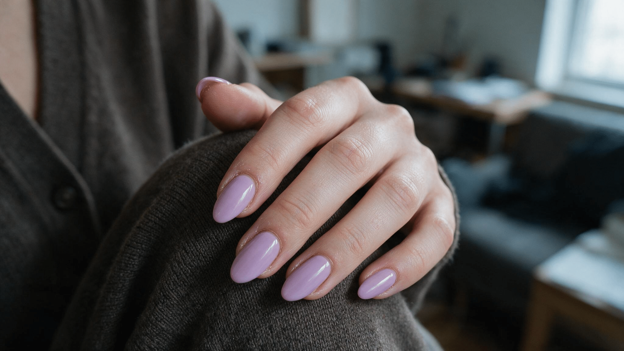 medium almond nails painted soft lilac with a glossy finish resting naturally across a neutral cardigan sleeve