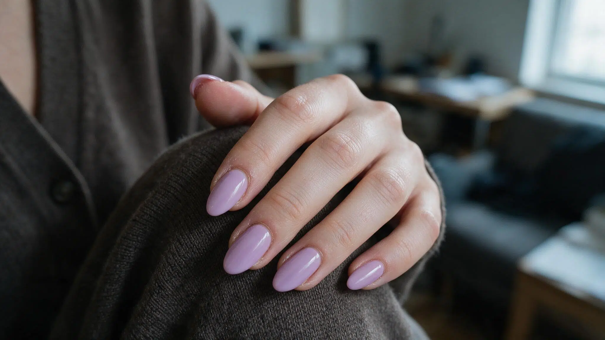 medium almond nails painted soft lilac with a glossy finish resting naturally across a neutral cardigan sleeve