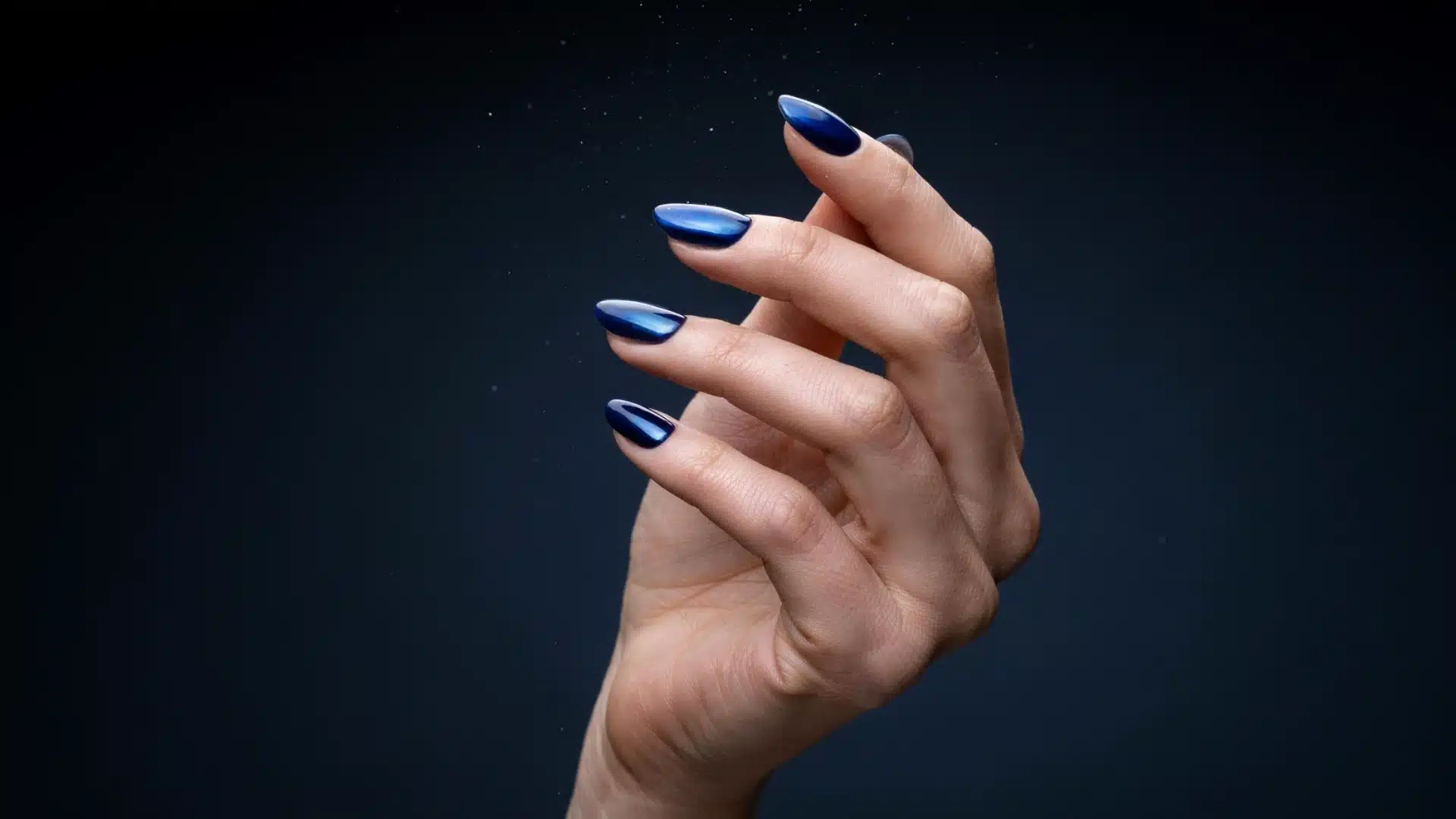 midnight blue chrome almond nails with glossy metallic shine on a natural hand against a dark background