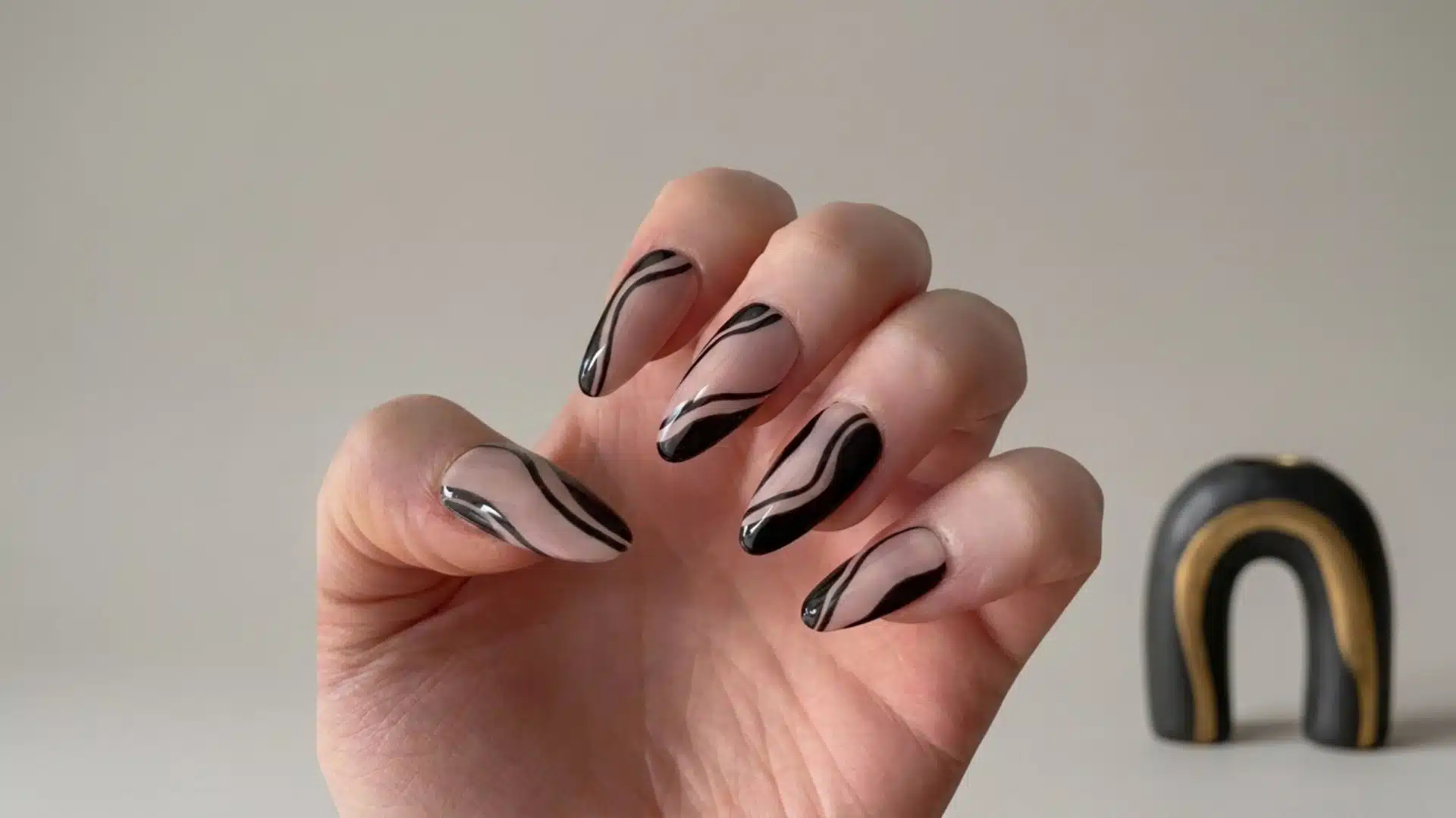 nude almond nails with glossy black swirl designs on a natural hand against a neutral background