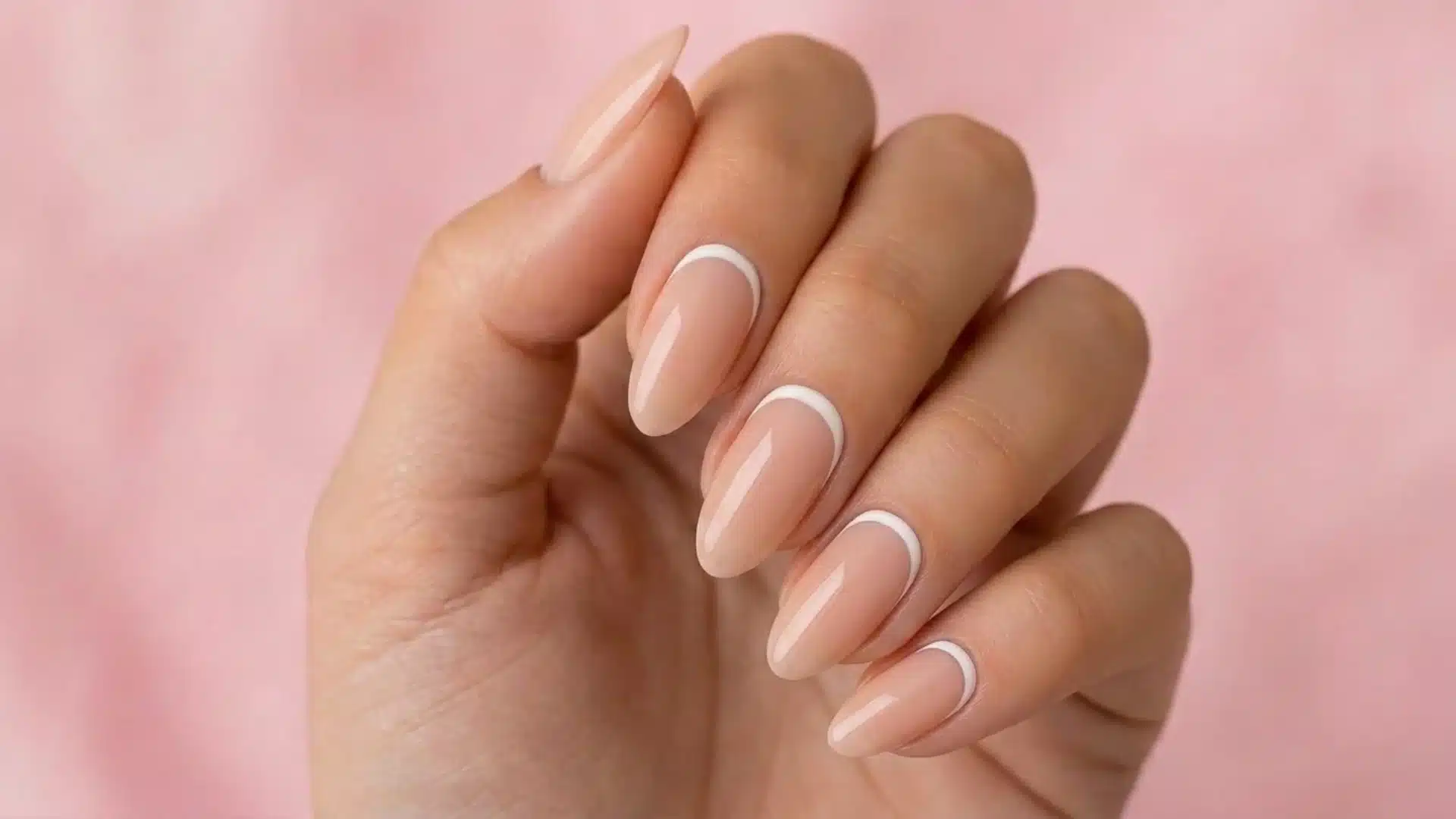nude almond nails with white reverse french tips on hand against soft pink background