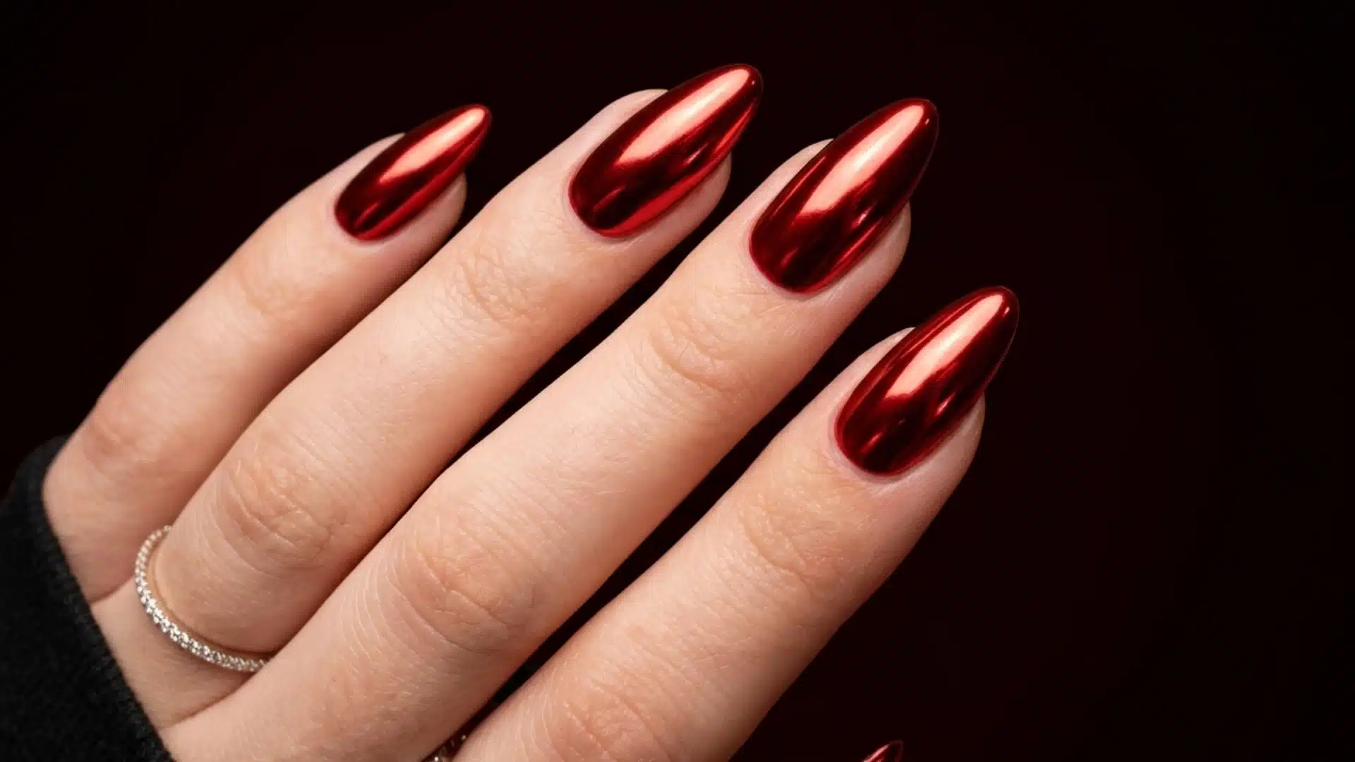 red chrome almond nails with a glossy mirror finish on a natural hand against a dark background