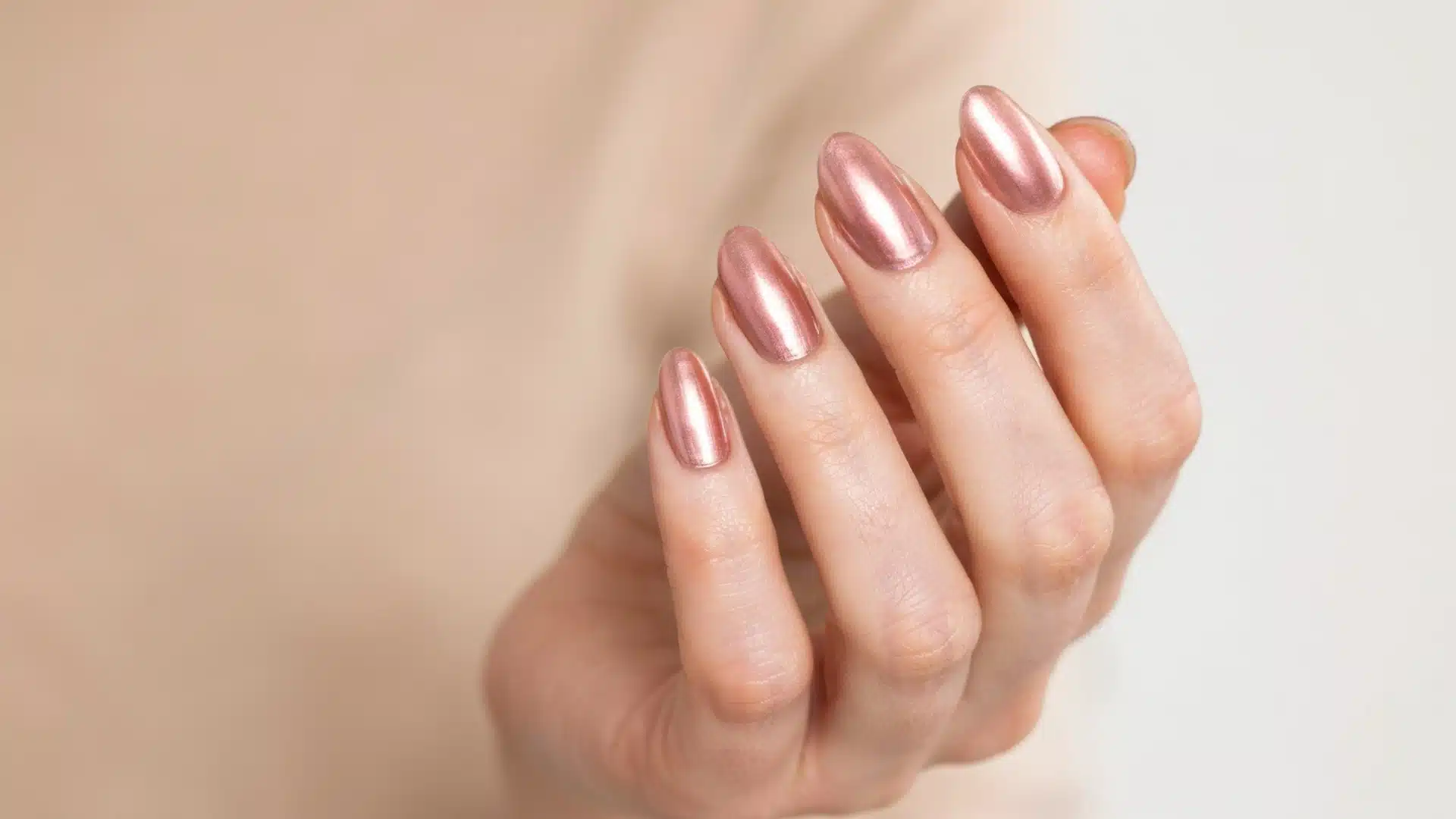 rose gold chrome almond nails with a smooth metallic finish on a natural hand against a soft neutral background