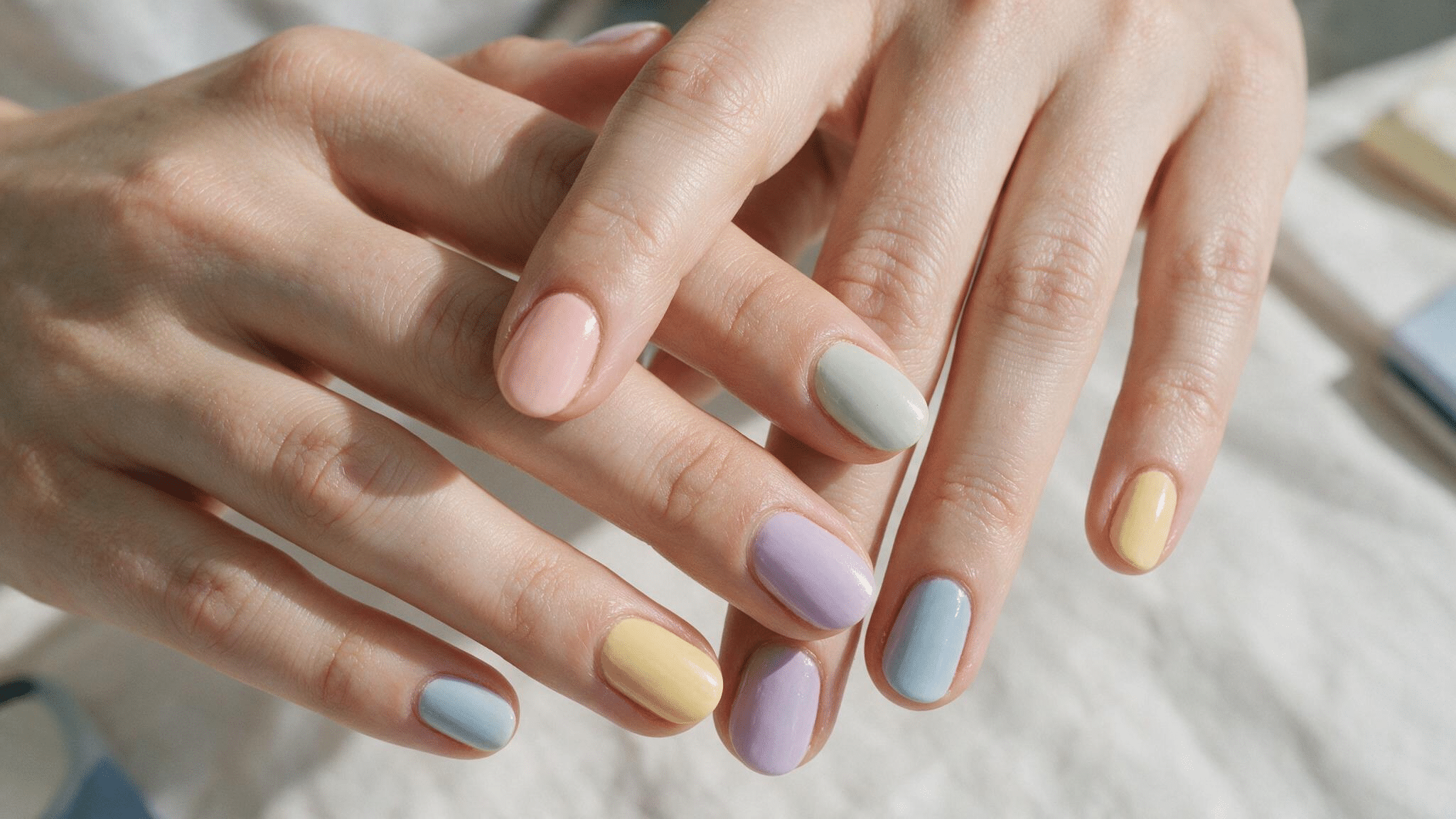 short oval nails each painted a different muted pastel shade including yellow pink mint lavender and pale blue
