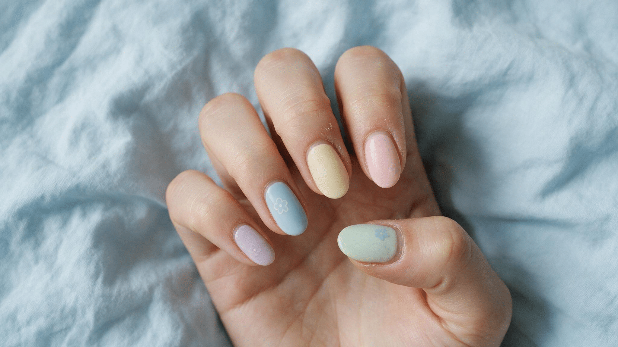 short oval nails in lilac butter yellow blue mint and blush pastel colors with tiny flower outlines on accent nails