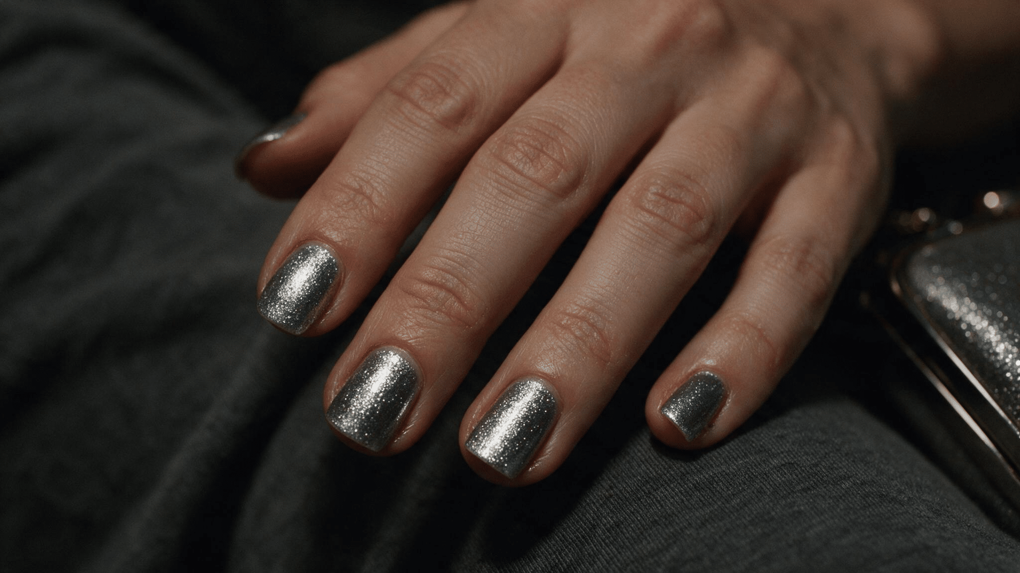 short squoval nails with cool platinum silver shimmer reflecting soft evening light while resting against dark gray fabric