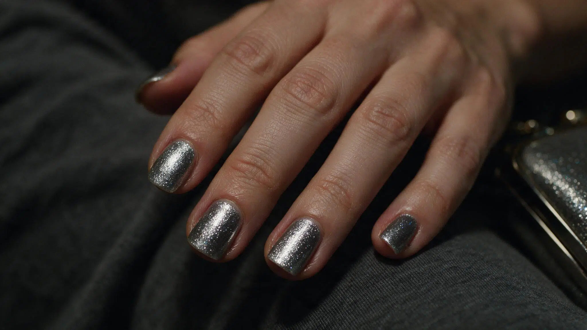 short squoval nails with cool platinum silver shimmer reflecting soft evening light while resting against dark gray fabric
