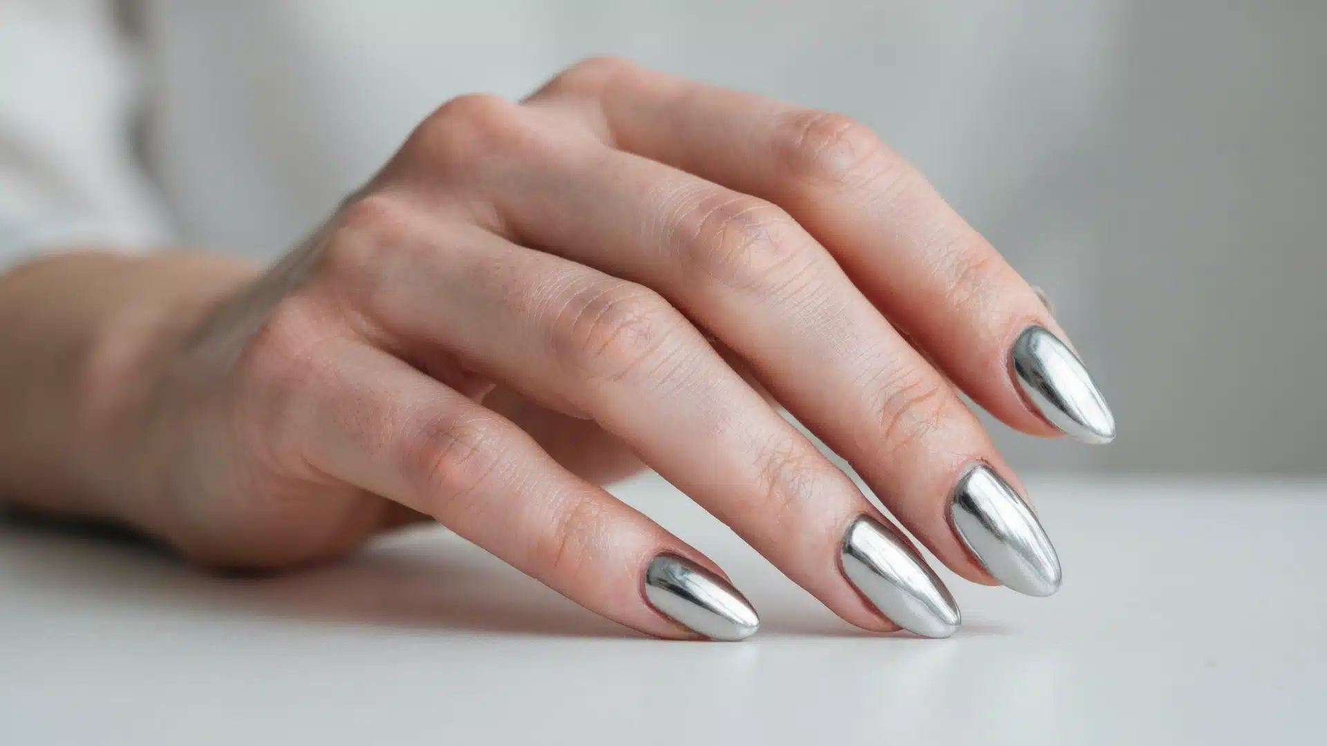 silver chrome almond nails with metallic mirror finish on hand against a soft neutral background