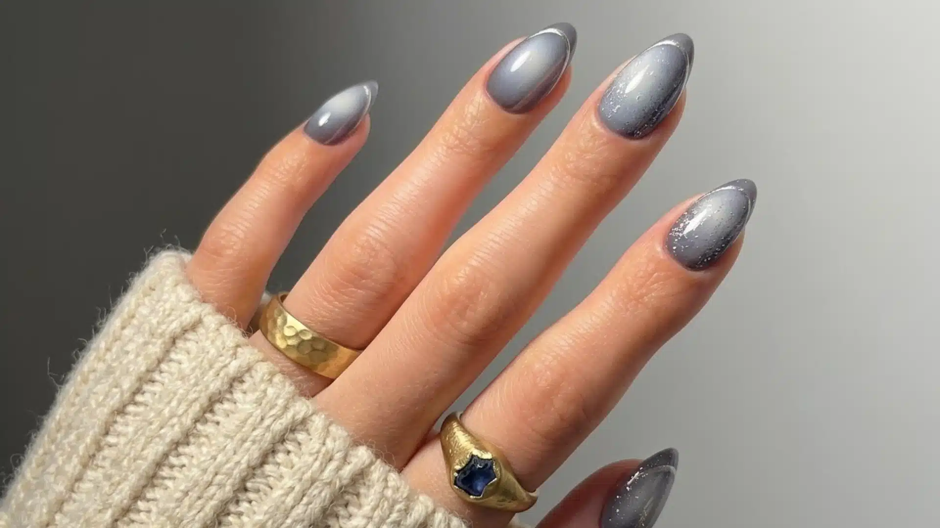 smoky gray almond nails with silver shimmer details and glossy finish on a natural hand with gold rings