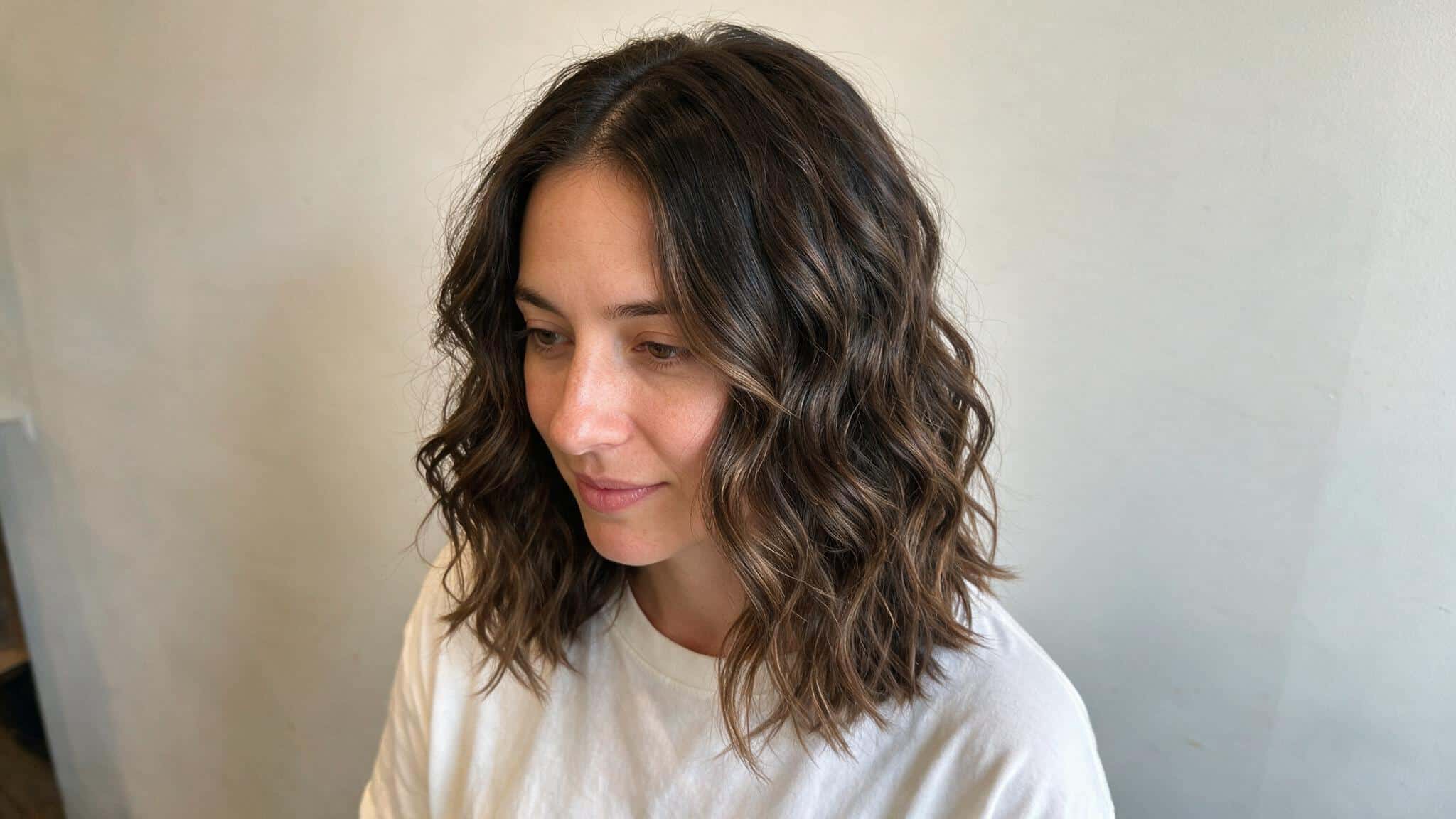 woman with medium brown body wave perm showing loose s shaped waves natural roots soft volume and layered salon textures