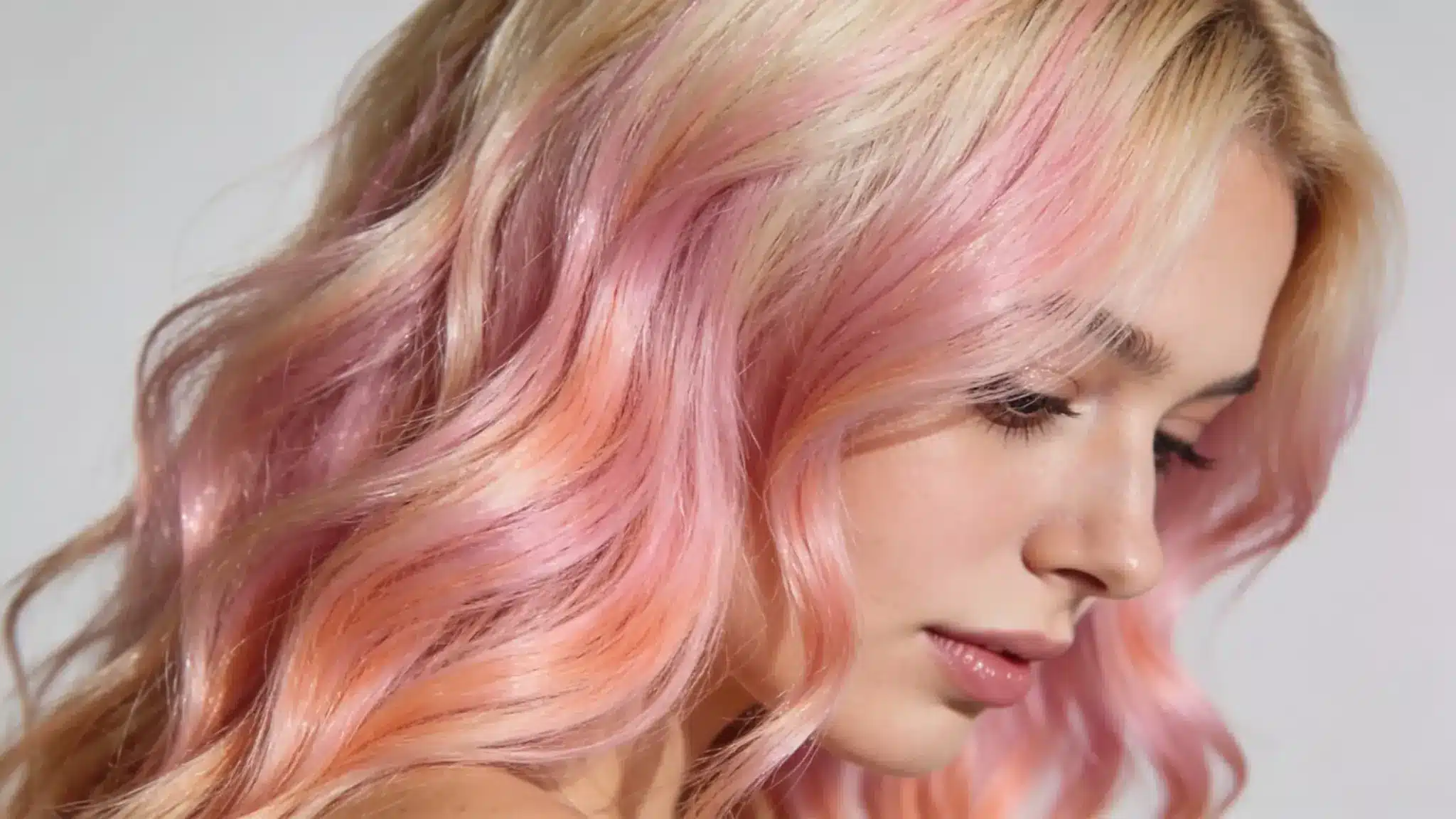 woman with rose gold balayage featuring soft pink peach tones on blonde wavy hair