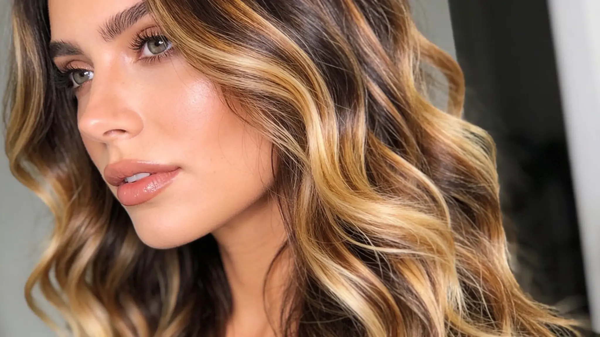 woman with wavy balayage hair featuring warm blonde highlights and dark brown tones