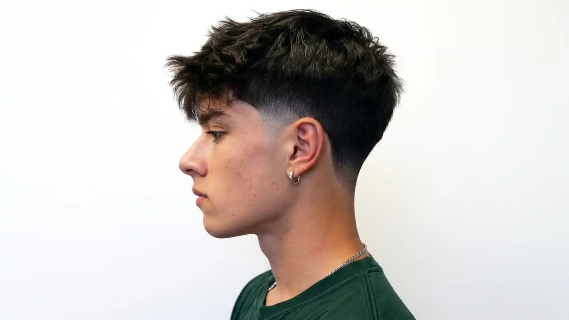 young man in side profile with a taper fade haircut textured dark hair and a silver hoop earring