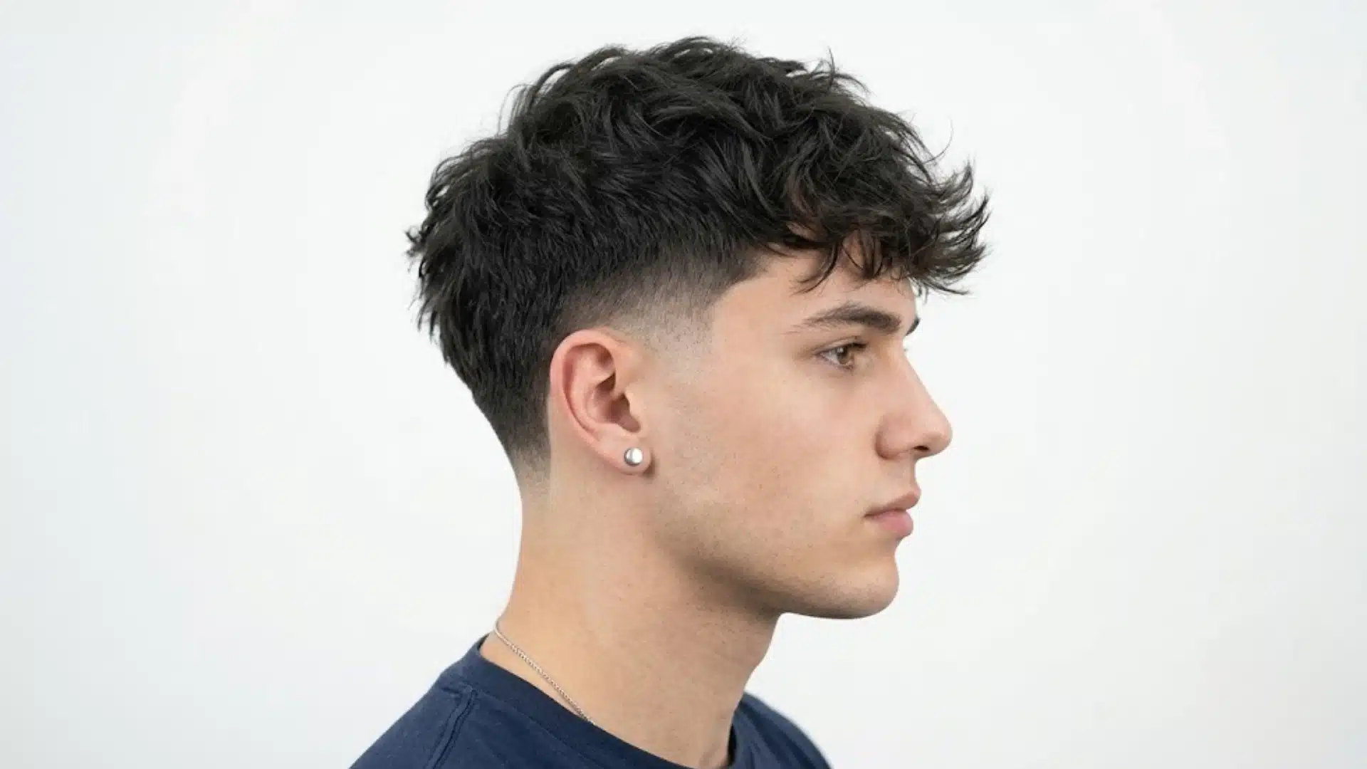 Young man with curly textured top and clean taper fade shown in side profile against plain background