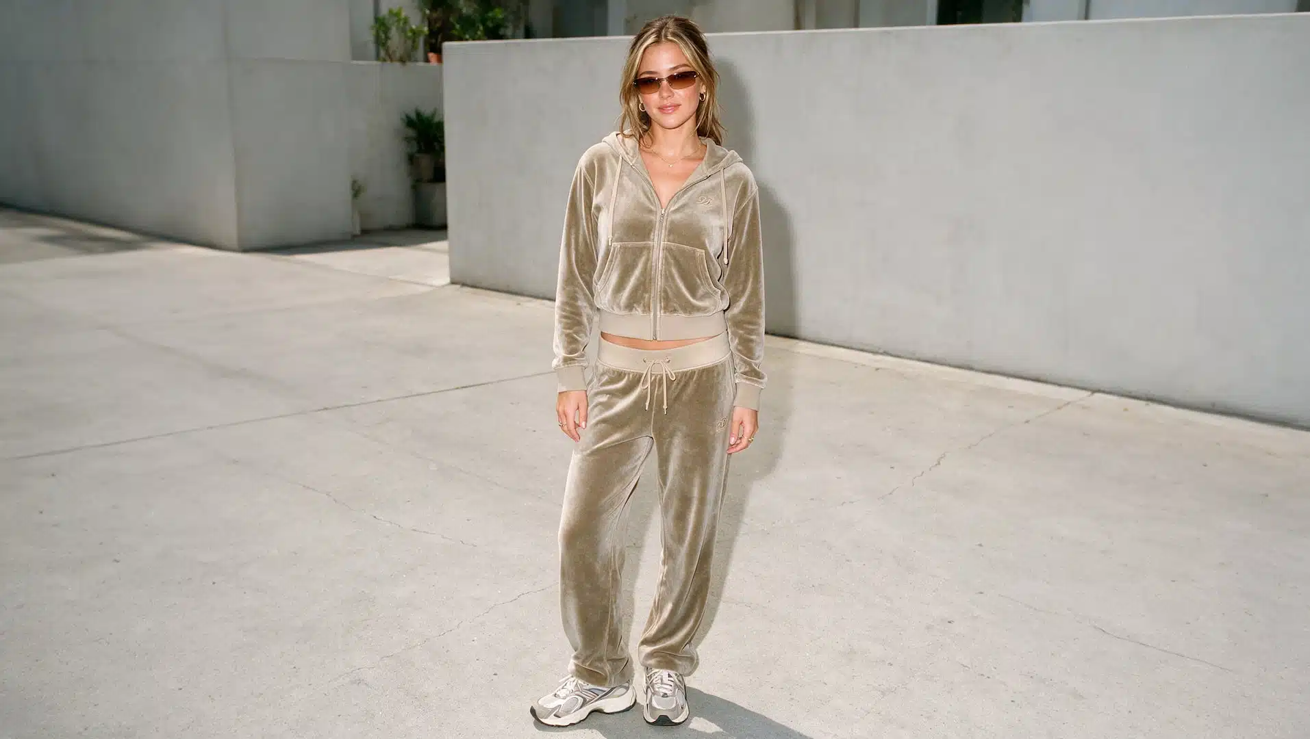 young woman in a velour tracksuit and chunky sneakers with tinted sunglasses in a y2k look