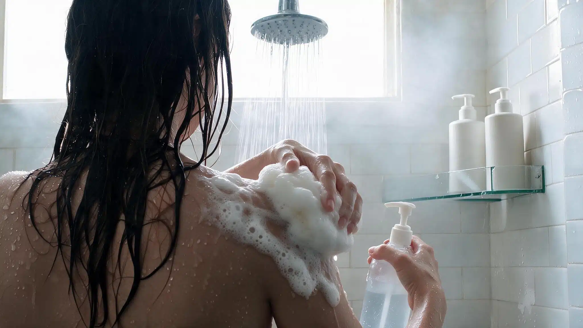 person using shower gel or body wash during a shower routine viewed from behind