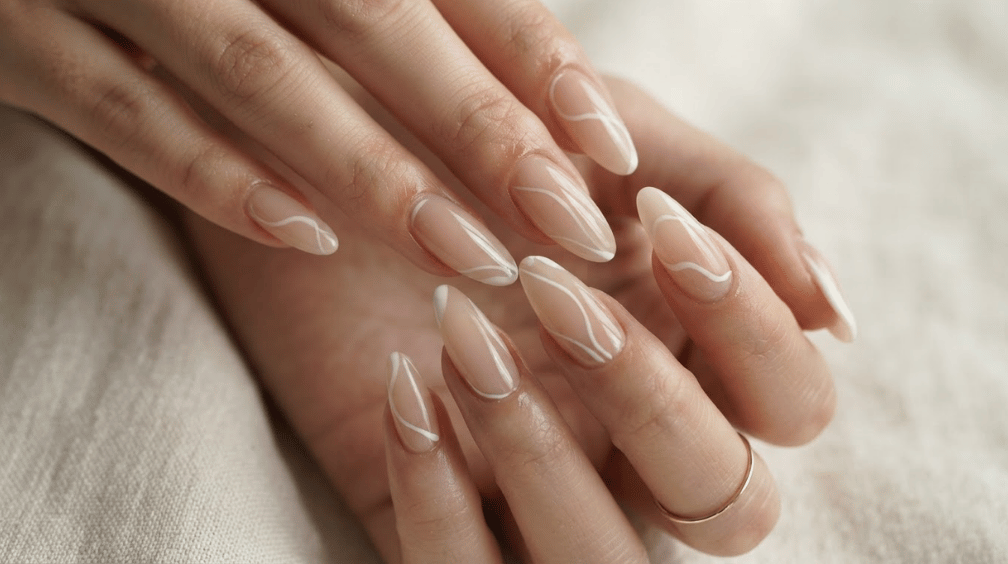 long almond nude nails decorated with delicate flowing white line art against soft cream fabric
